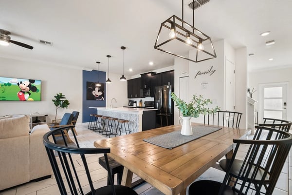 Open-plan kitchen and dining area with wooden table, black chairs, black cabinetry, and blue accent wall with Mickey Mouse artwork