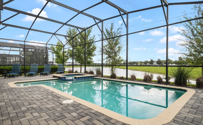 Screened-in swimming pool with turquoise water, lounge chairs, and waterfront view of green lawn and trees
